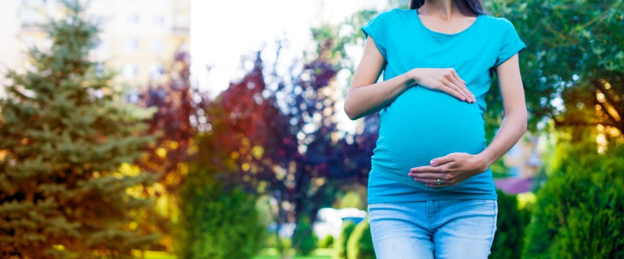 Waiting for the baby. A young pregnant woman in the background of the park holds her hands behind her belly